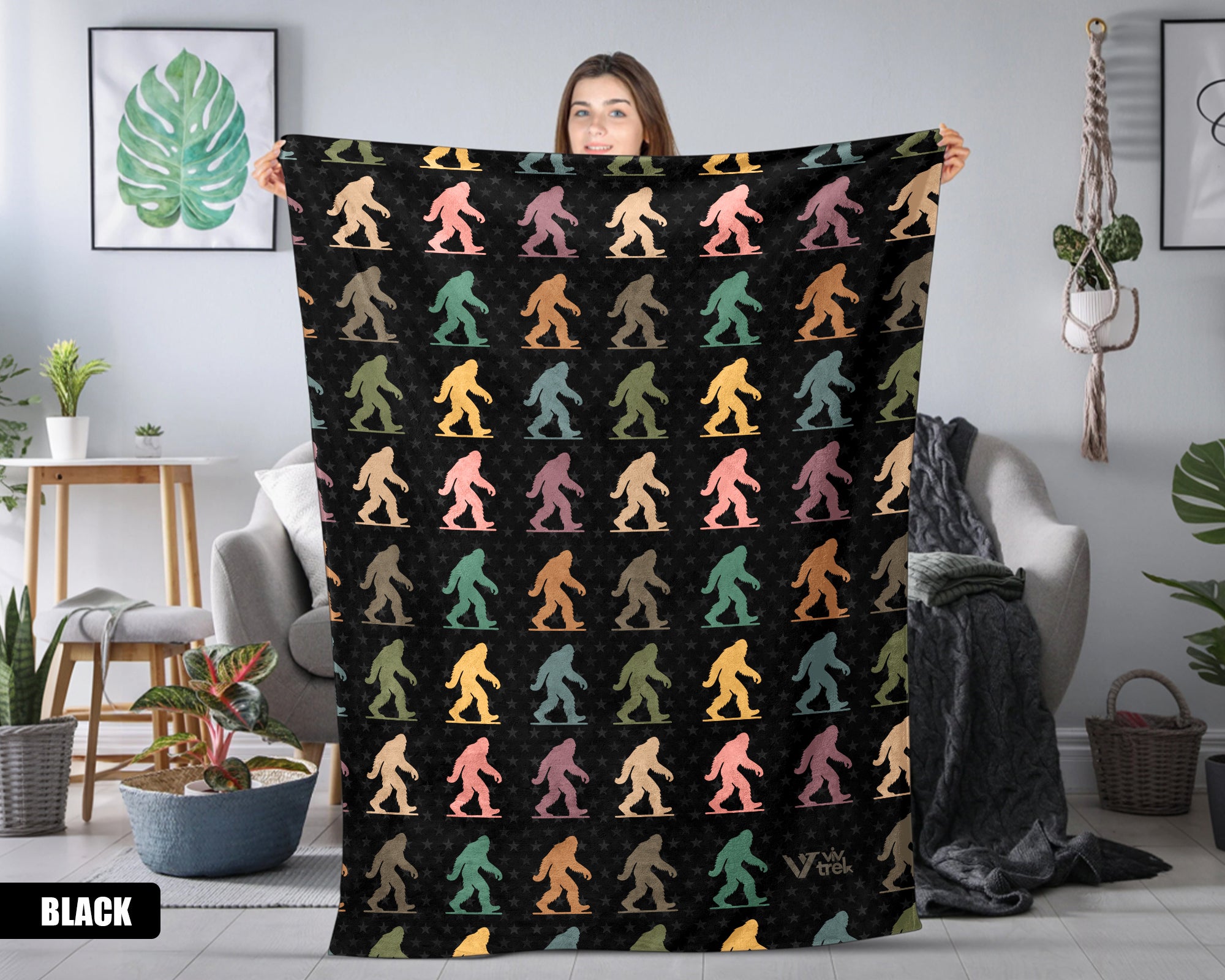 Person holding a black blanket with colorful bigfoot pattern in a room.