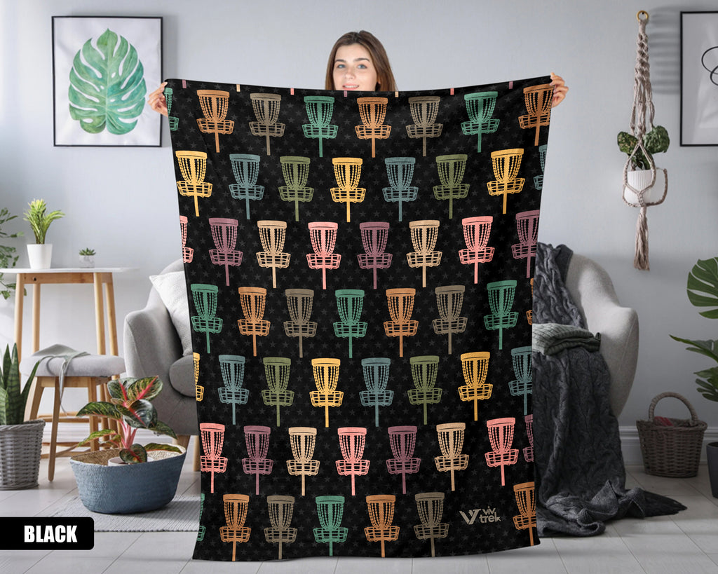 Person holding a black blanket with colorful disc golf basket pattern in a room.
