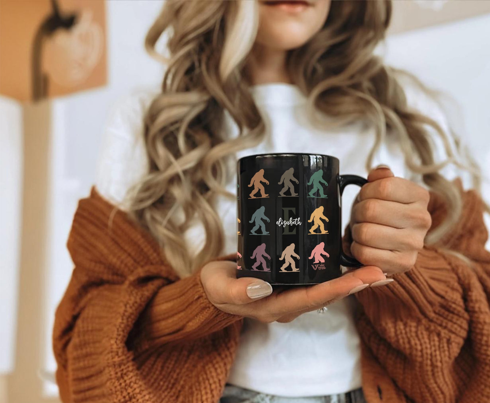 Person holding a black mug with colorful bigfoot designs and name text