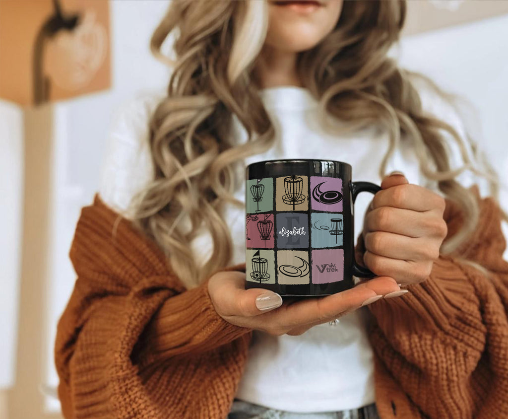 Person holding a black mug with colorful designs and name text