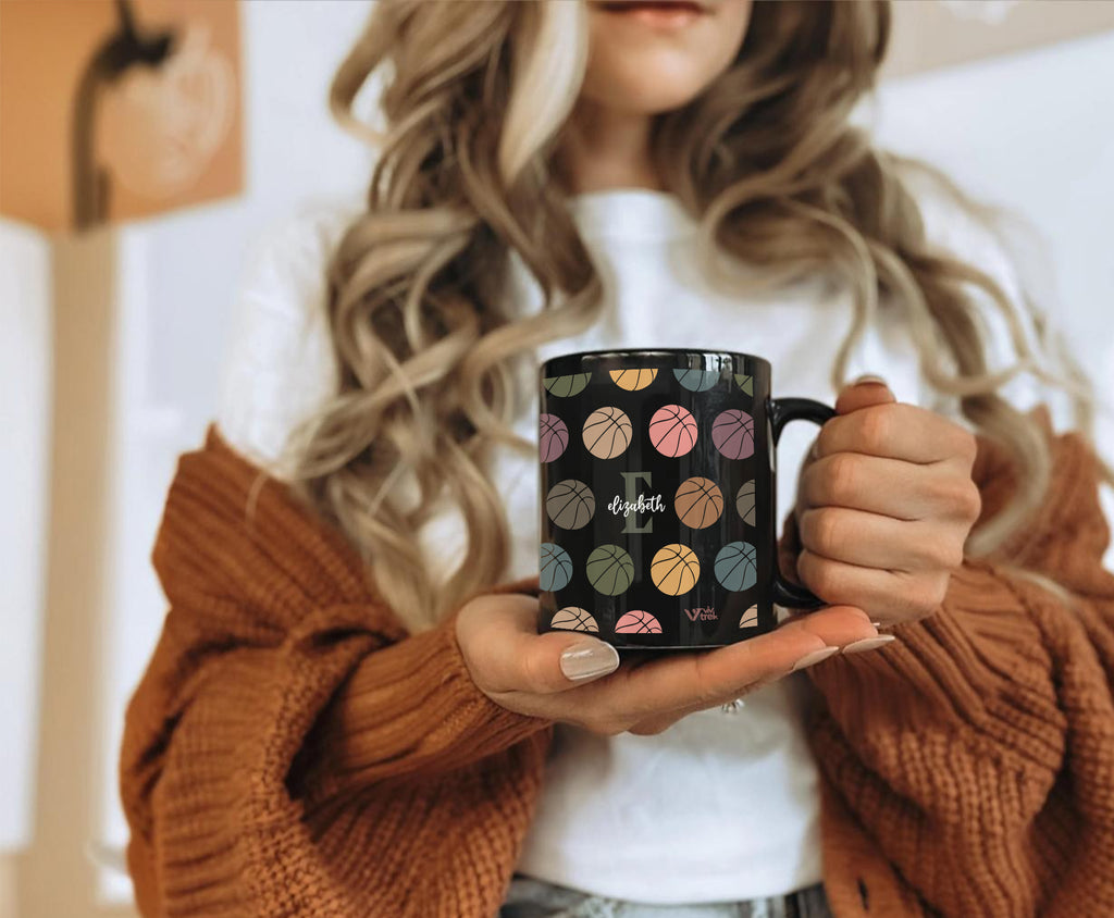 Person holding a black mug with colorful patterns and the letter text on it.