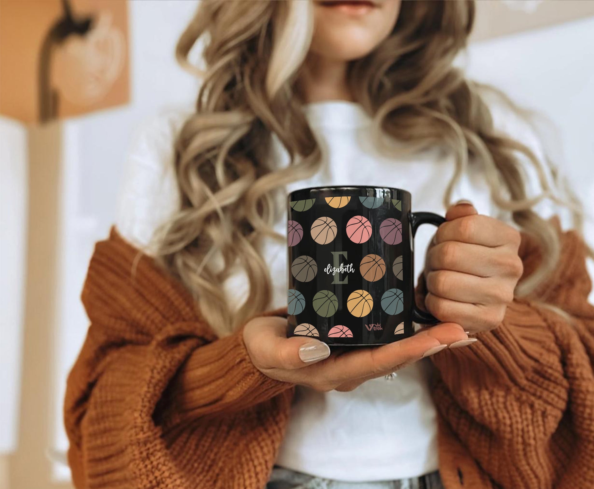 Person holding a black mug with colorful patterns and the letter text on it.