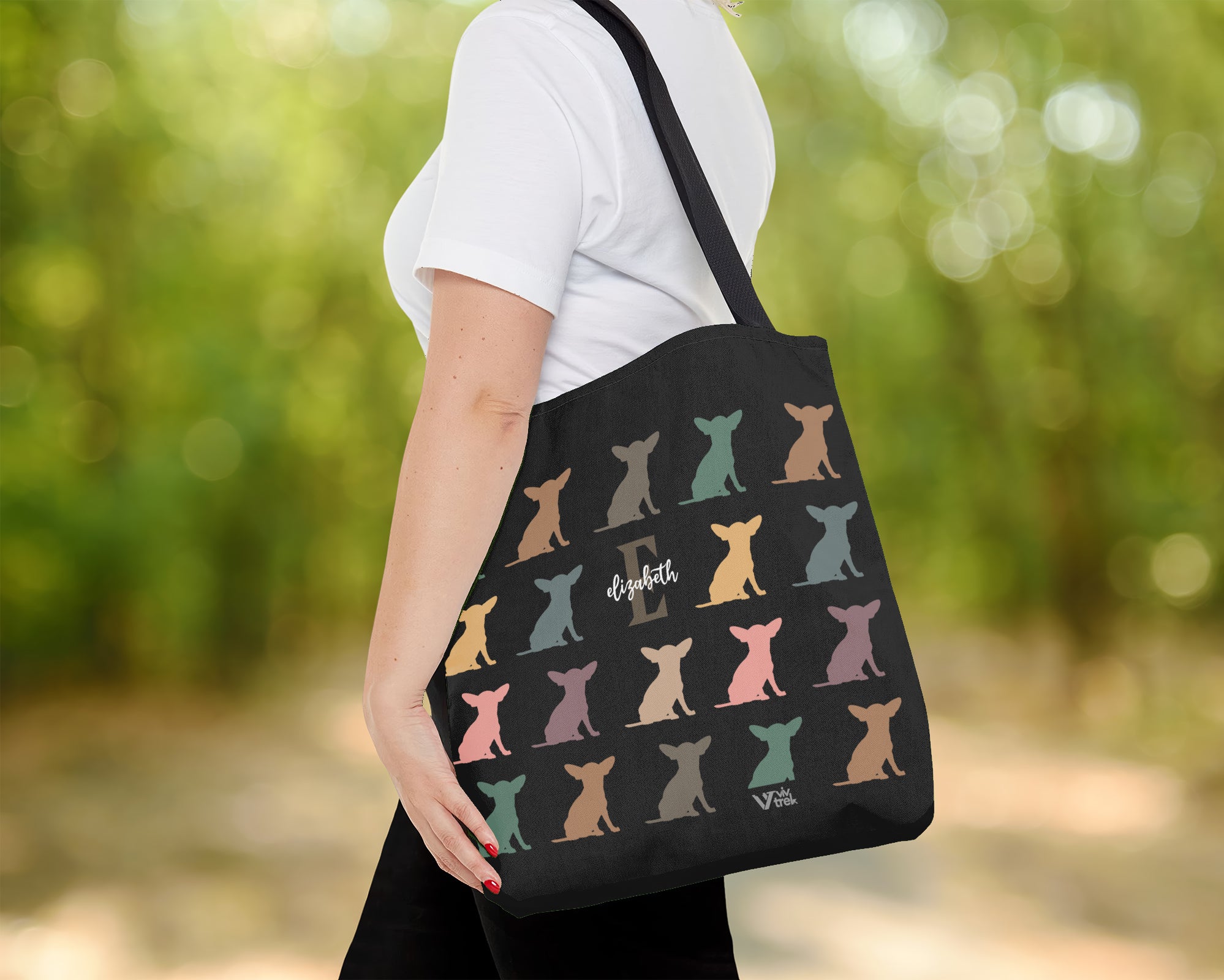 Person holding a black tote bag with colorful dog pattern outdoors and initial name text