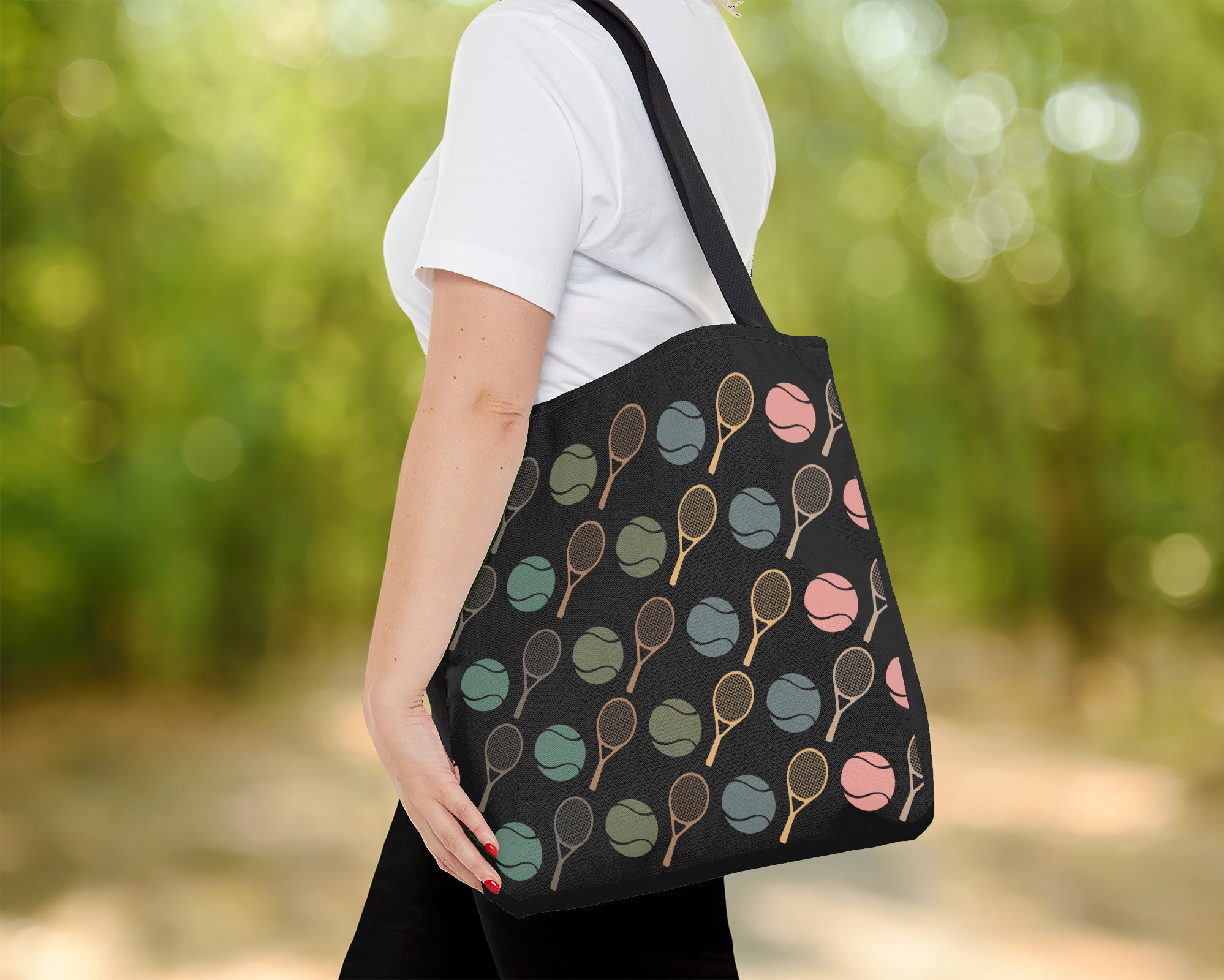 Person holding a black tote bag with colorful tennis racket pattern outdoors.
