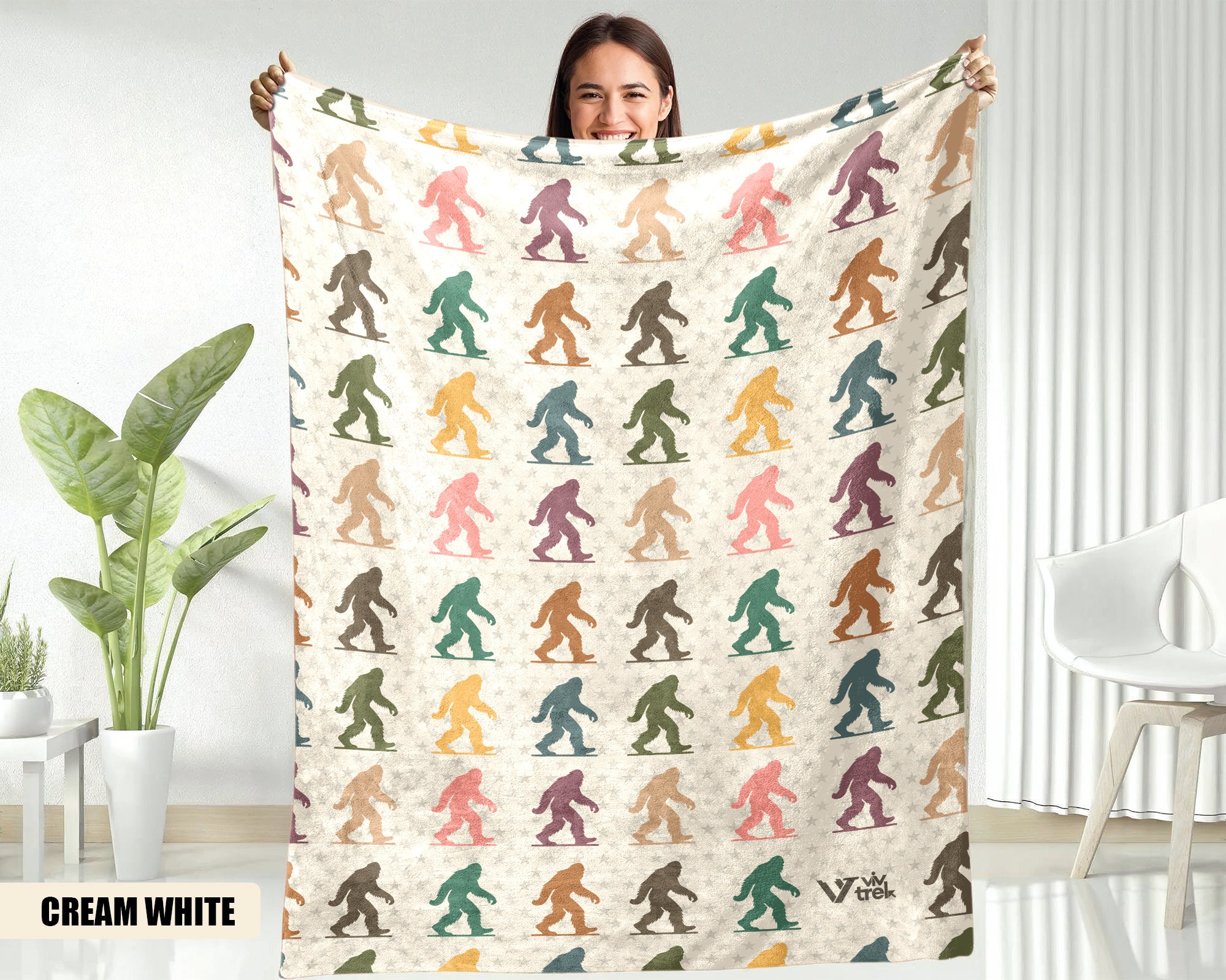 Person holding a blanket with colorful bigfoot pattern in a room with plants and furniture.