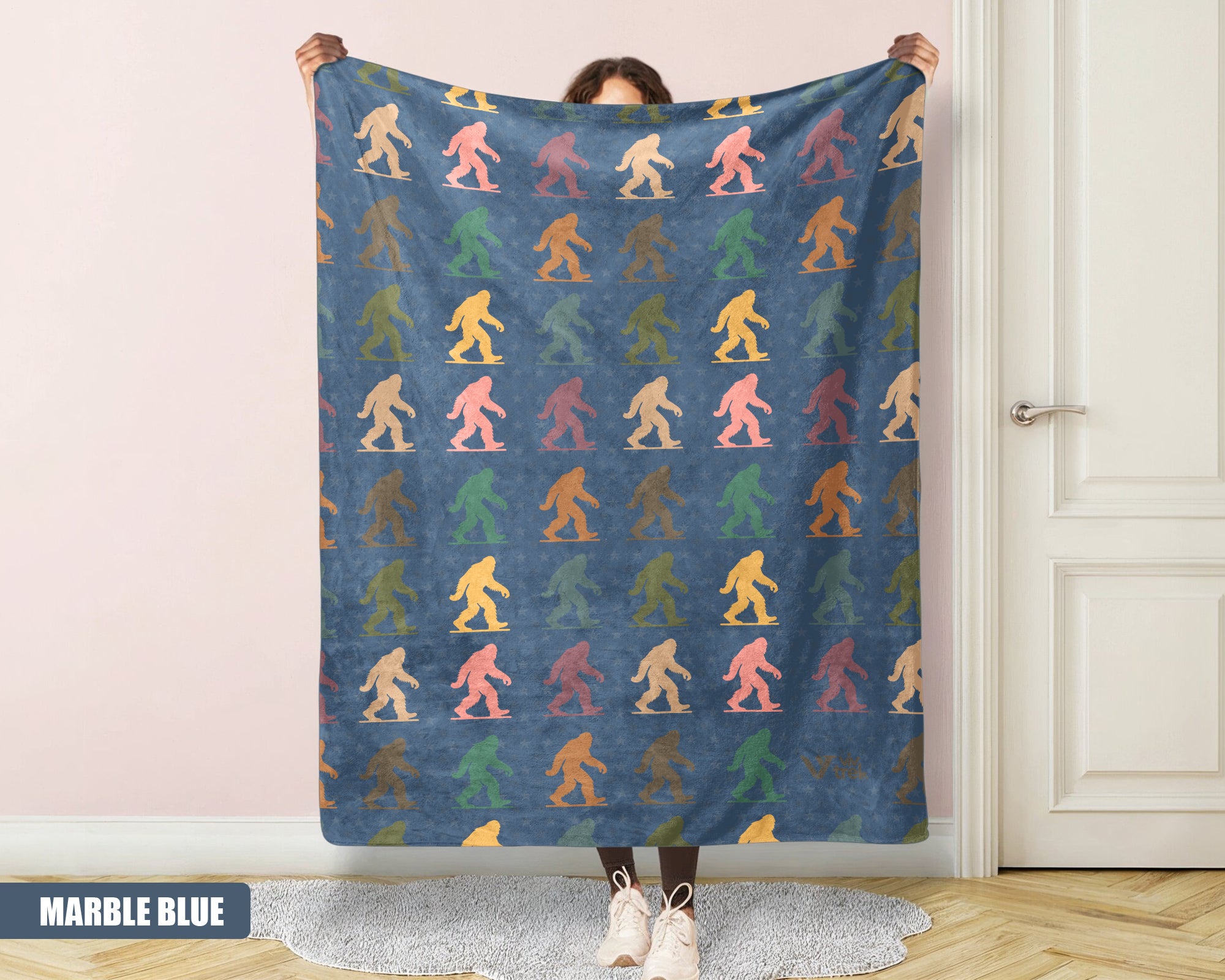 Person holding a colorful 'Bigfoot' pattern blanket with a marble blue background.