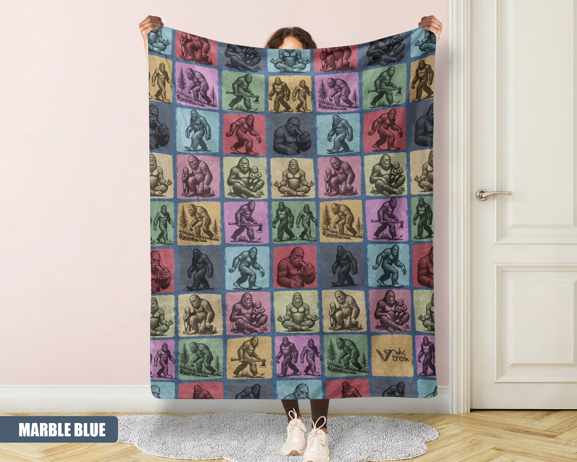 Person holding a colorful blanket with a pattern of Bigfoot in a room.