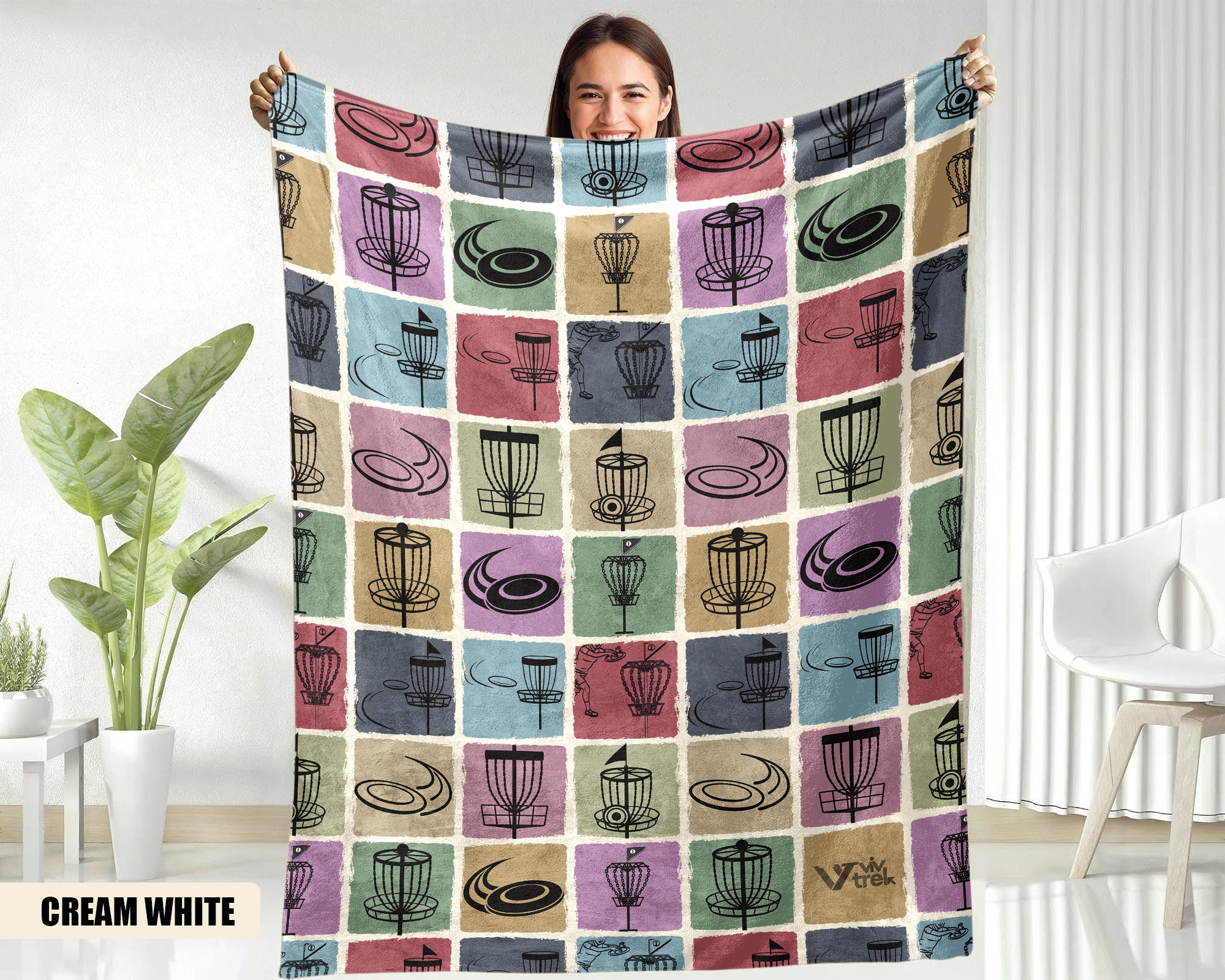 Person holding a colorful disk golf blanket with coffee-themed patterns in a room with a plant and chair.