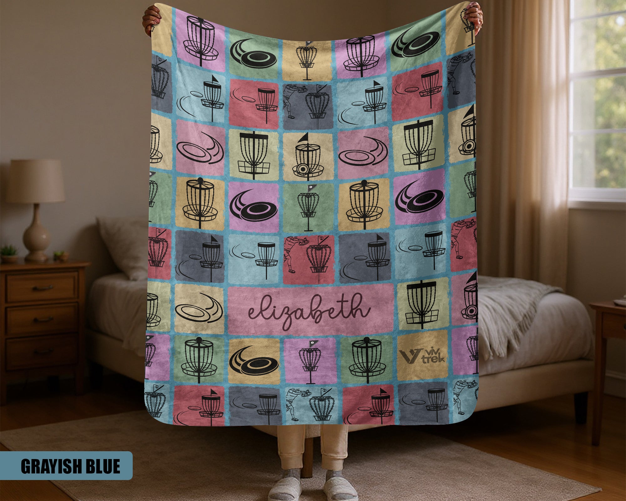 Person holding a colorful quilt with pattern and name name in a bedroom setting.