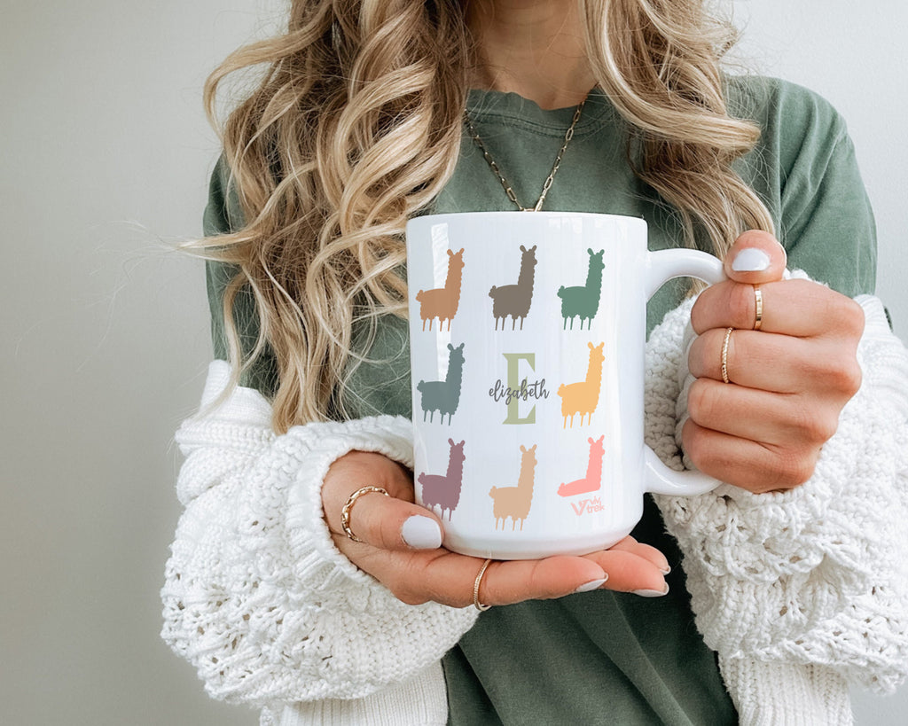 Person holding a mug with colorful llama designs and the word name on a light background