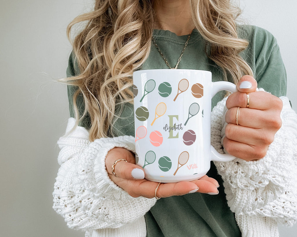 Person holding a mug with tennis racket design and letter.