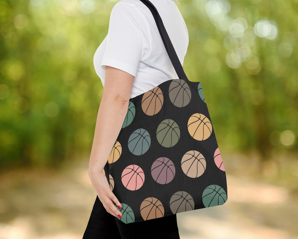 Person holding a tote bag with colorful basketball pattern against a blurred green background