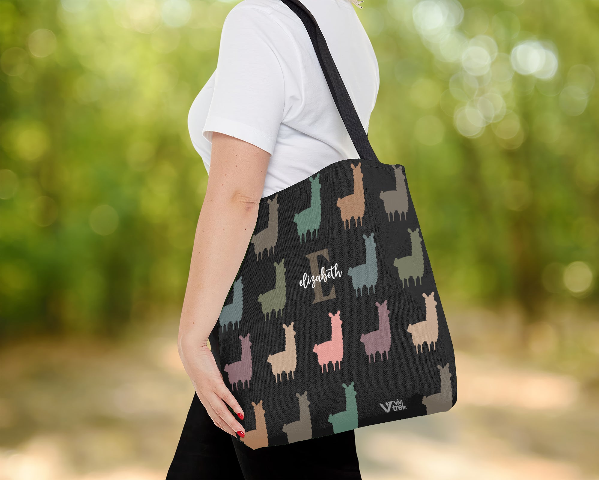 Person holding a tote bag with llama pattern and name with branding outdoors.