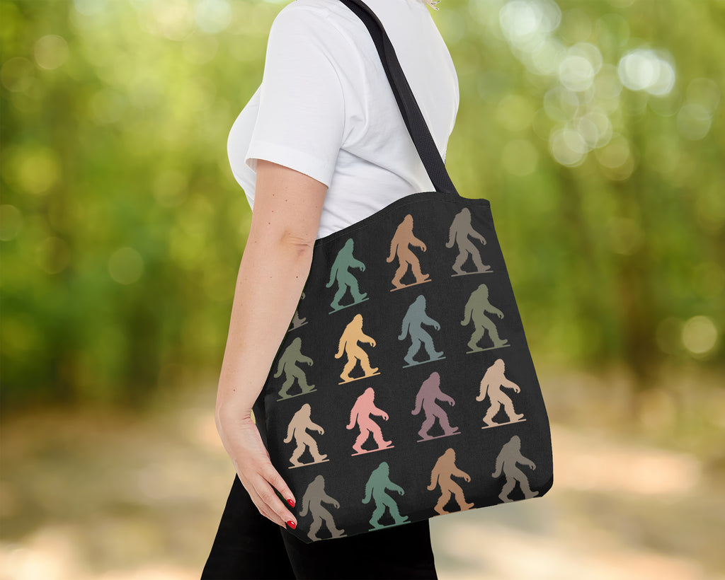 Tote bag with colorful bigfoot silhouettes held by a person outdoors.